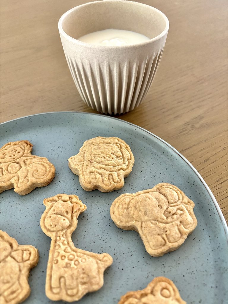 animal shaped sourdough discard animal crackers on a blue plate with a small cup of milk on a brown wooden table