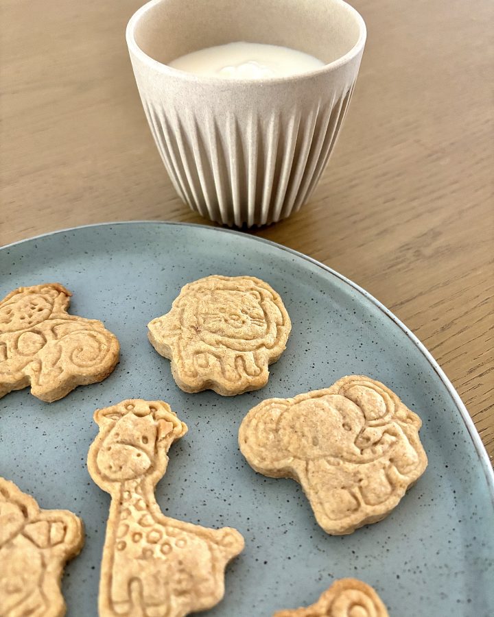 sourdough discard animal shaped crackers on a round blue plate with a cup of milk on a brown table