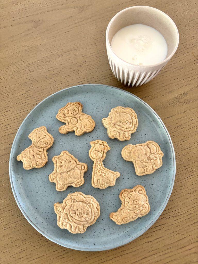 overhead view of assorted animal shaped sourdough discard animal crackers on a blue plate with a cup of milk on a brown table